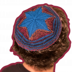 A man is shown from behind, from the shoulders up. He has a black shirt, and brown curly hair that covers his ears. He is wearing a brown and burgundy kippah, with a blue Star of David on the crown.